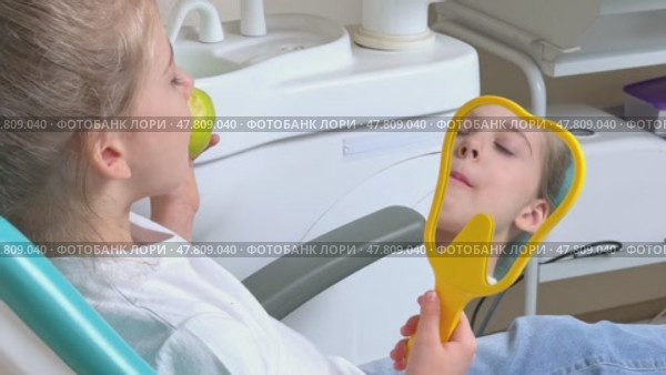 Little girl are eating green apple in the dentist's chair and looking in the mirror at her teeth. Healthy teeth concept. Child eat a green apple. Slow motion footage. Стоковое видео, видеограф Ирина Михайличенко / Фотобанк Лори