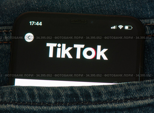 Логотип TikTok ("ТикТок") на экране мобильного телефона, лежащего в кармане джинсов (крупный план) (2020 год). Редакционное фото, фотограф E. O. / Фотобанк Лори