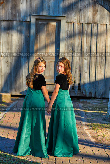 Long dress twin teen sisters hand in hand at the park sooden cabin. Стоковое фото, агентство Ingram Publishing / Фотобанк Лори