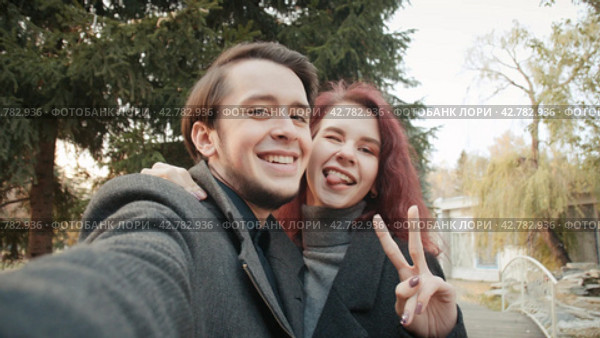 Lovely young couple is taking photo themselves outdoors in the autumn city park. Стоковое видео, видеограф EStarodubov / Фотобанк Лори