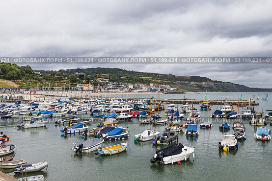 Lyme Regis Harbour with Moored Boats and Beachfront. Lyme Regis, UK, 3 July 2024. Редакционное фото, фотограф Zydrius Tartenis / Фотобанк Лори