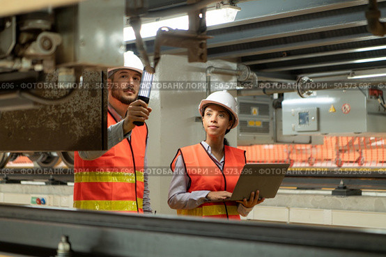 Male and female engineers work together in an electric repair station. Inspecting the undercarriage of electric train that are being repaired at the garage. Стоковое фото, агентство Ingram Publishing / Фотобанк Лори