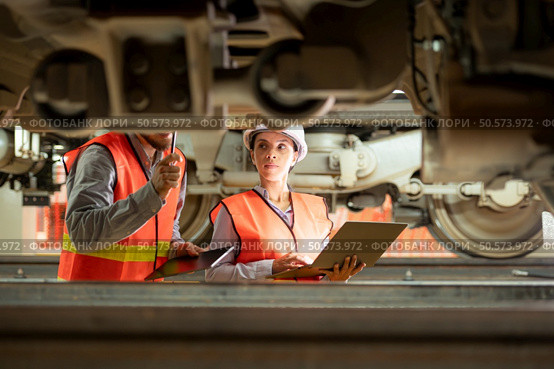 Male and female engineers work together in an electric repair station. Inspecting the undercarriage of electric train that are being repaired at the garage. Стоковое фото, агентство Ingram Publishing / Фотобанк Лори
