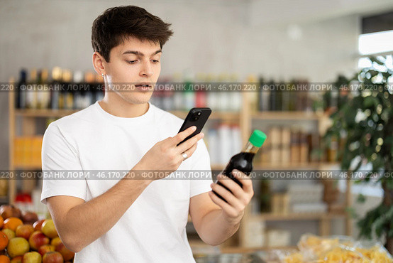Male buyer checks suitability - scans QR code on jar of soy sauce label in grocery store. Стоковое фото, фотограф Яков Филимонов / Фотобанк Лори