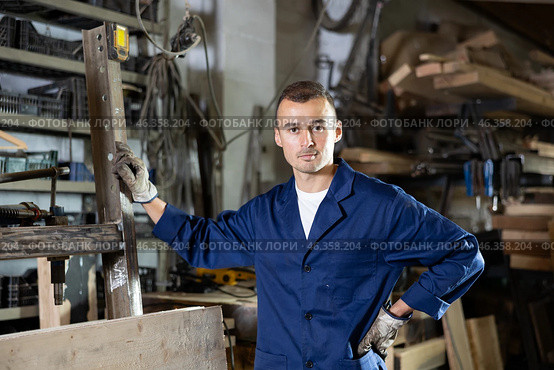 Male employee of workshop stands next to iron rails of workpieces, measures length. Стоковое фото, фотограф Яков Филимонов / Фотобанк Лори