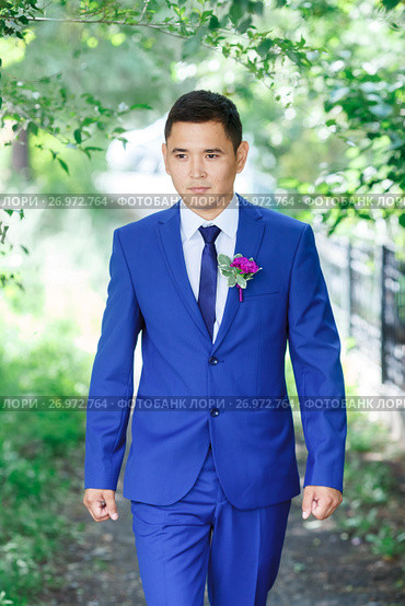 Male model, the groom portrait in a blue suit with a boutonniere among the green foliage on a wedding day. Стоковое фото, фотограф Евгений Майнагашев / Фотобанк Лори
