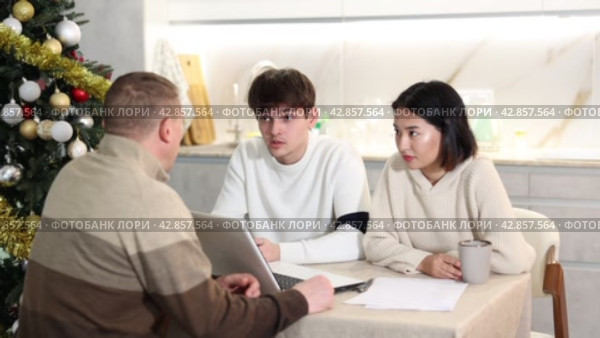 Male realtor discusses the terms of contract with couple in office of real estate agency, offering various accommodation options against backdrop of a Christmas tree. Стоковое видео, видеограф Яков Филимонов / Фотобанк Лори