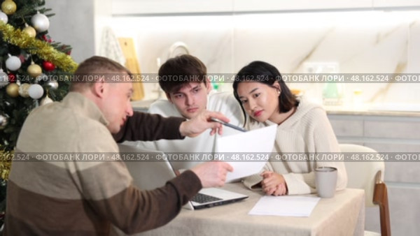 Male realtor discusses the terms of contract with couple in office of real estate agency, offering various accommodation options against backdrop of a Christmas tree. Стоковое видео, видеограф Яков Филимонов / Фотобанк Лори