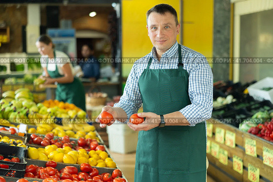 Male seller of vegetable department of store replenishing showcase with tomato, put ones on showcase. Стоковое фото, фотограф Яков Филимонов / Фотобанк Лори