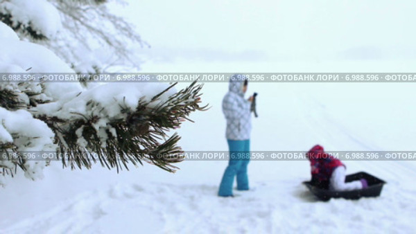 Мама с дочкой фотографируются на льду зимнего озера. Фокус на заснеженную ветку ели. Стоковое видео, видеограф Кекяляйнен Андрей / Фотобанк Лори