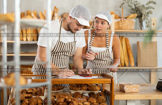 Man and woman sellers in bakery make calculations, work with paper documents and count using phone. Стоковое фото, фотограф Яков Филимонов / Фотобанк Лори