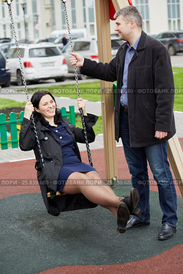 Man and woman spend time riding on chain swing at playground. Стоковое фото, фотограф Losevsky Pavel / Фотобанк Лори