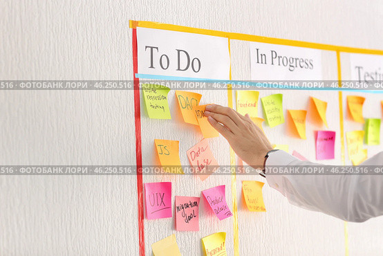 Man attaching sticky note to scrum task board in office. Стоковое фото, фотограф Pixel_shot / Фотобанк Лори