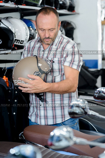 man choosing motorcycle helmet in dealers showroom. Стоковое фото, агентство Ingram Publishing / Фотобанк Лори