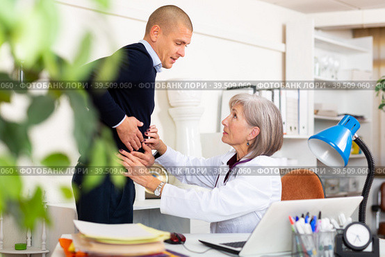 Man complaining about stomach ache to mature woman physician. Стоковое фото, фотограф Яков Филимонов / Фотобанк Лори