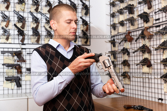 Man examining sporting revolvers before buying in gun store. Стоковое фото, фотограф Яков Филимонов / Фотобанк Лори