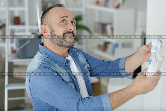man holding colour charts looking round room. Стоковое фото, агентство Ingram Publishing / Фотобанк Лори