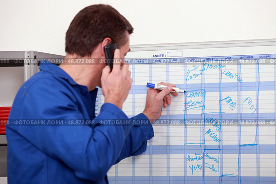 Man in blue overalls talking on the phone and writing on a board. Стоковое фото, агентство Ingram Publishing / Фотобанк Лори