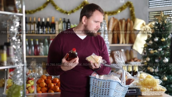 Man is interested in choosing cheese and whiskey in a supermarket decorated for Christmas. Buyer chooses alcohol and snacks. Стоковое видео, видеограф Яков Филимонов / Фотобанк Лори