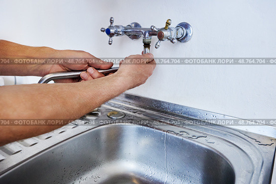 Man is replacing wall-mounted faucet spout using hands without tools while water traces remain near sink on metal countertop. Стоковое фото, фотограф Владимир Григорьев / Фотобанк Лори