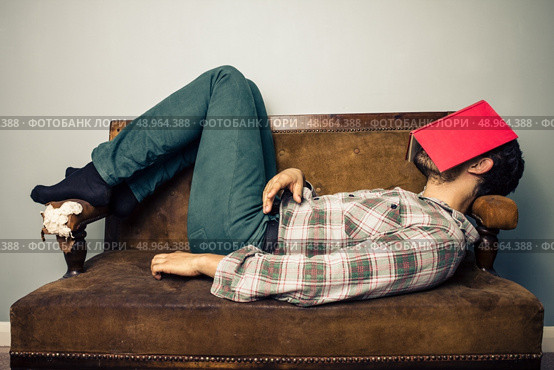 Man on sofa with book on his face. Стоковое фото, агентство Ingram Publishing / Фотобанк Лори