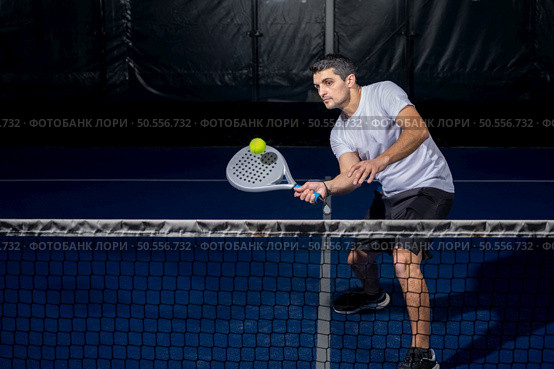 Man playing padel in a blue indoor padel court padel - Young sporty boy padel player hitting ball with a racket. Стоковое фото, агентство Ingram Publishing / Фотобанк Лори