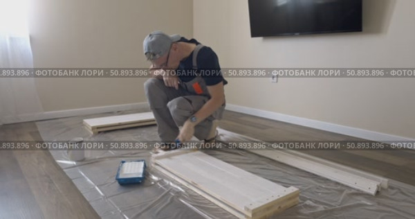 Man Professional carpenter painting wooden boards with white paint using roller brush in modern interior room during home renovation construction. Painting of wooden shelving. furniture assembly. Стоковое видео, видеограф Сергей Тимофеев / Фотобанк Лори