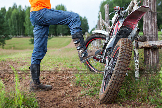 Man rider standing near dirt motorcycle in countryside, steps with boot on bike peg. Стоковое фото, фотограф Кекяляйнен Андрей / Фотобанк Лори