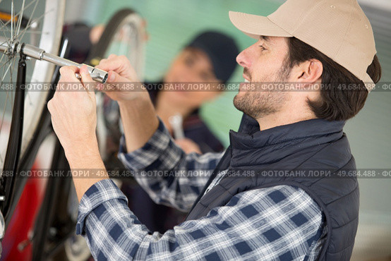 man tightening axle on bicycle wheel using a socket wrench. Стоковое фото, агентство Ingram Publishing / Фотобанк Лори