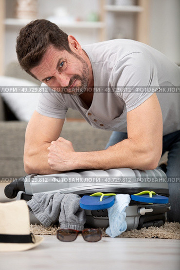 man trying to fit all clothing to packing his suitcase. Стоковое фото, агентство Ingram Publishing / Фотобанк Лори