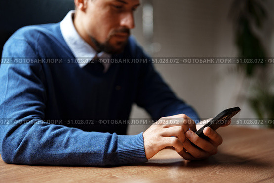Man using smartphone while sitting at a wooden desk in a modern office during daytime. Стоковое фото, фотограф Сергей Толмачёв / Фотобанк Лори
