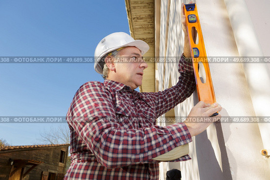 Man using spirit level on exterior wall. Стоковое фото, агентство Ingram Publishing / Фотобанк Лори