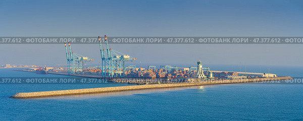 Manama, Bahrain - Jan 08 2024, Panoramic view of Bahrain commercial international  port with blue cranes, pier, buildings and containers, with sea on foreground, at daytime, Manama, Bahrain. Редакционное фото, фотограф Сергей Богомяко / Фотобанк Лори