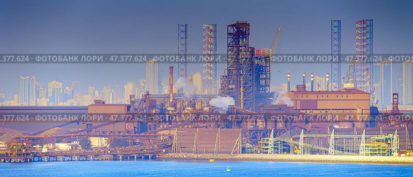 Manama, Bahrain- Jan 08 2024, Panoramic view of the industrial port buildings, constructions, the skyscrapers of Manama are visible in the distance, in the daytime, Manama, Bahrain. Редакционное фото, фотограф Сергей Богомяко / Фотобанк Лори