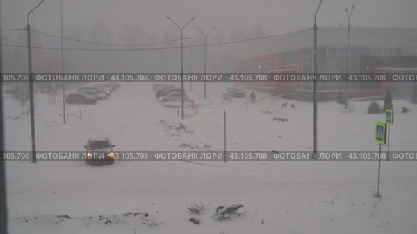 Машины медленно выезжают с парковки у городского бассейна весной во время заморозков и сильной снежной метели в городе Петрозаводске (2024 год). Редакционное видео, видеограф Sergei Gorin / Фотобанк Лори