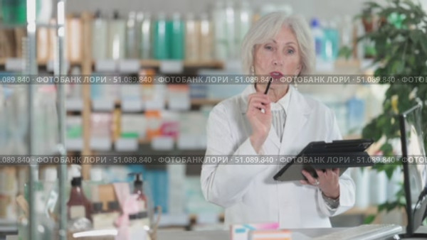 Mature female pharmacist works with a stylus on a tablet, she counts the leftovers of drugs in the pharmacy warehouse and plans a restock. Pharmacist works in a pharmacy. Стоковое видео, видеограф Яков Филимонов / Фотобанк Лори