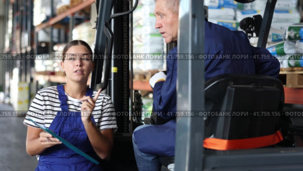Mature man drive operate automatic fork lift loader and answers young female auditors questions. Стоковое видео, видеограф Яков Филимонов / Фотобанк Лори