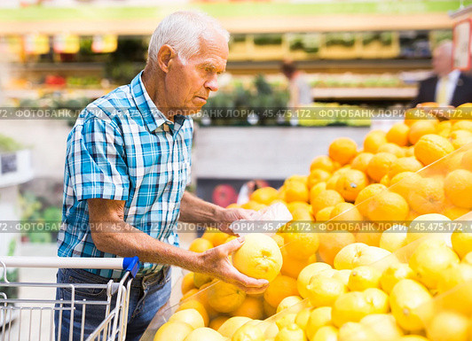 Mature senor examines oranges in fruit section of supermarket. Стоковое фото, фотограф Татьяна Яцевич / Фотобанк Лори