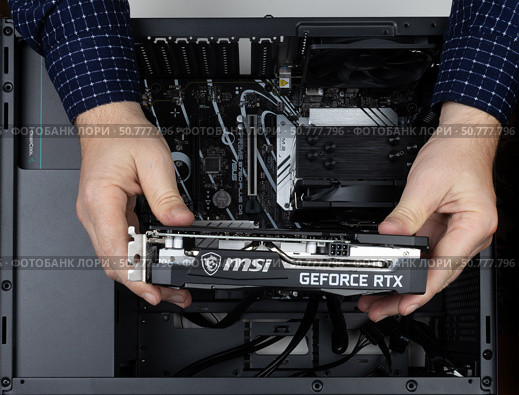 Maykop, Russia - February 18, 2025: Man assembling computer, holding new msi geforce rtx graphics card over asus motherboard in system unit. Редакционное фото, фотограф Андрей С / Фотобанк Лори