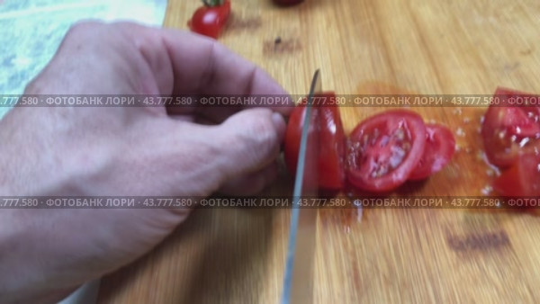 Men's hands are slicing cherry tomatoes on a wooden board with a large kitchen knife. Стоковое видео, видеограф Ярославский Максим / Фотобанк Лори