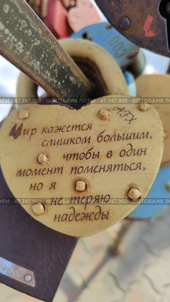 Металлический навесной замок с философской надписью "мир кажется слишком большим, чтобы в один момент поменяться, но я не теряю надежды". Замок на металлической конструкции в сквере Семьи на левом берегу реки Орлик. Редакционное фото, фотограф Ирина / Фотобанк Лори