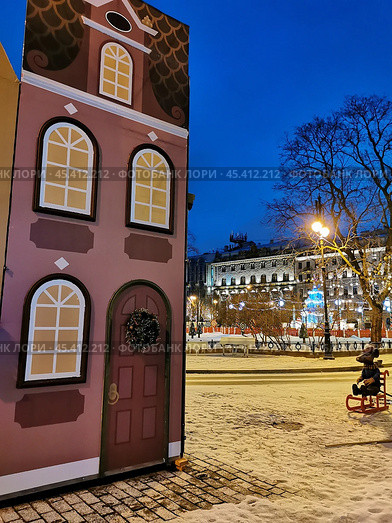 Между нарисованными домами сидит мышь на красных санках, потом белое пианино, рядом стол с белой скатертью на рождественской в стиле Щелкунчика ярмарке на Манежной площади в Петербурге ранним утром (2021 год). Стоковое фото, фотограф Елена Яворская / Фотобанк Лори