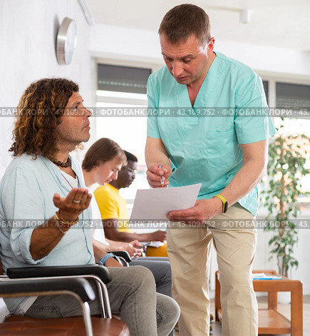 Middle-aged male doctor and visitor sitting on bench discussing medical document. Стоковое фото, фотограф Яков Филимонов / Фотобанк Лори