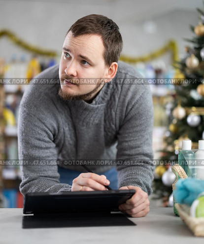 Middle-aged man restocking using tablet in store with New Year decoration. Стоковое фото, фотограф Яков Филимонов / Фотобанк Лори