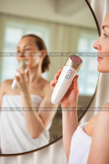 Middle-aged Woman Rejuvenates Her Skin Using Innovative Electrical Device in Serene Indoor Setting. Стоковое фото, фотограф Aleksandr Golubev / Фотобанк Лори