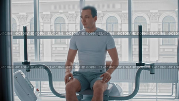 Modern gym - a guy sitting down on the training apparatus and waiting for when it will be possible to start. Стоковое видео, видеограф Константин Шишкин / Фотобанк Лори