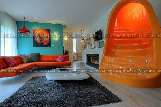 Modern living room interior in retro-futurism style with bright color accents. The central place is occupied by an orange plastic staircase of unusual shape, leading to the second floor. The interior is complemented by a stylish modular sofa of coral color, abstract painting, a carpet with a long pile and a smooth coffee table. The room also has a fireplace and designer lighting. The space is filled with light, creativity and playfulness - ideal for interior design themes, architecture and stylish city life. Стоковое AI-изображение, AI-художник Анна Кривицкая / Фотобанк Лори