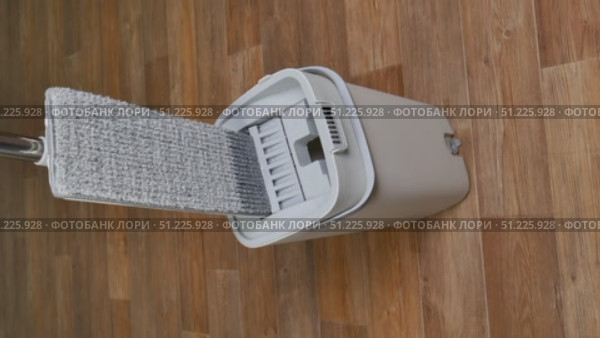 Modern mop is wrung out from water in gray bucket for washing floors on brown floor, cleaning concept household chores. Стоковое видео, видеограф Катерина Белякина / Фотобанк Лори