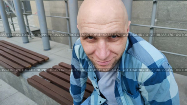 Молодой человек смотрит в камеру исподлобья. Забавный лысый парень в клетчатой рубашке ухмыляется. Красивый мужчина сидит на скамейке и улыбается, глядя краем глаза в камеру. Крупный план, портрет. The young man looks at the camera from under his brows. Funny bald guy in a plaid shirt is grinning. A handsome man is sitting on a bench and smiling, looking out of the corner of his eye at the camera. Close-up, portrait. Стоковое видео, видеограф Ирина / Фотобанк Лори