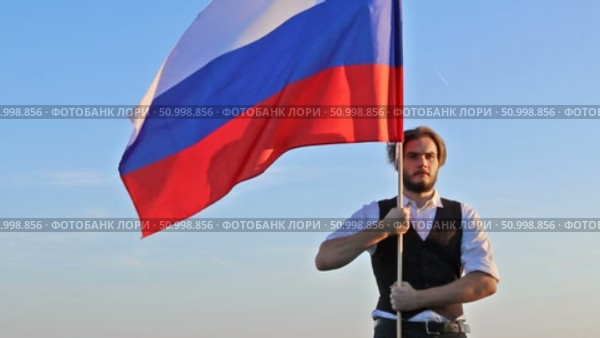 Молодой мужчина с российским флагом на фоне голубого неба. Стоковое видео, видеограф 1Andrey Милкин / Фотобанк Лори